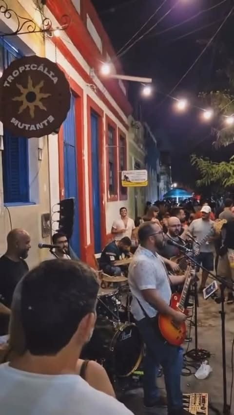 A calçada de noite, mesas cheias e luz quente saindo de dentro