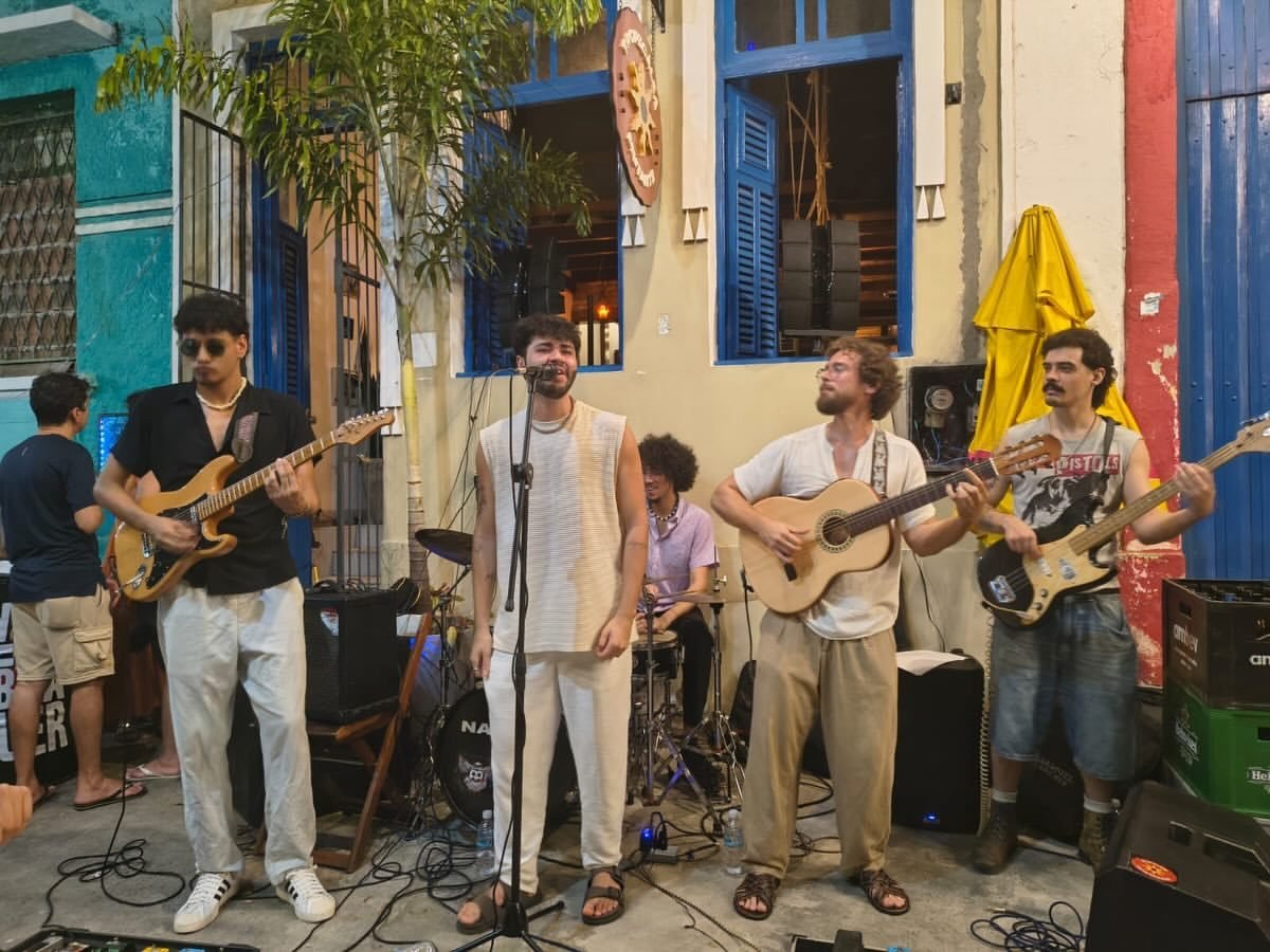 Músicos tocando na calçada, de frente para as mesas